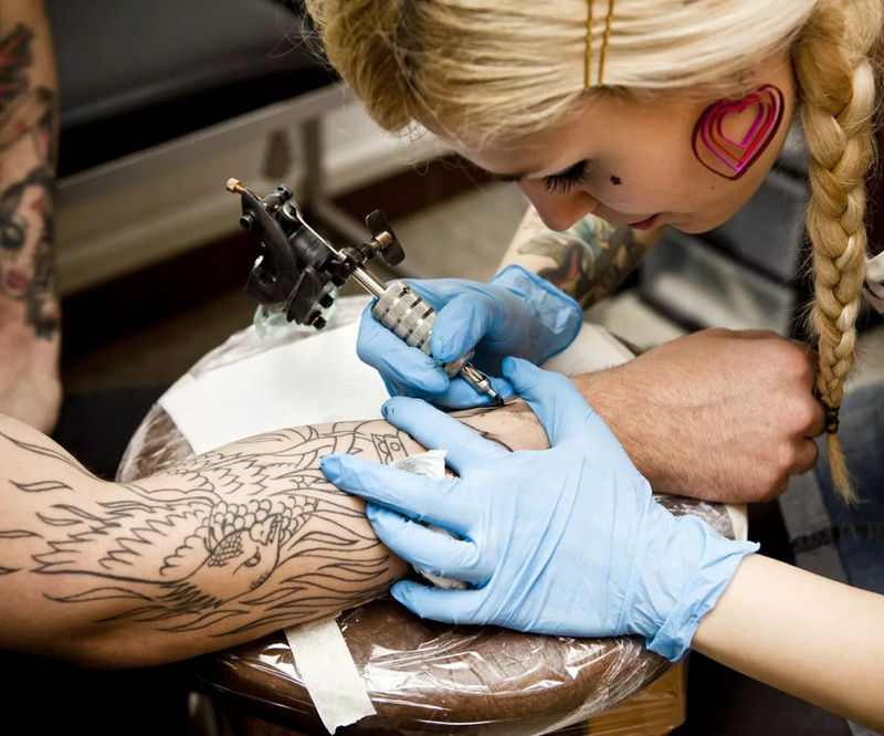 Девушка делает татуировку на руке парня